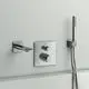Chromfarbener Wandthermostat von Ideal Standard mit separaten Bedienelementen für Temperatur und Wasserdurchfluss, kombiniert mit einer Handbrause und einem Wasserhahn.